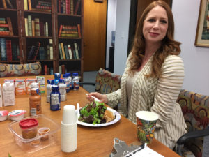 Nutritional Supplements for Eating Disorder Recovery - Katie Grubiak, RDN [image description: photo of Katie Grubiak sitting at table with lunch and several supplemental shakes]