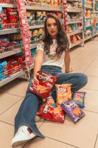 Person with ARFID [Image description: photo of a woman wearing jeans sitting on the floor of a supermarket with several small bags of assorted chips] Represents a potential patient with ARFID in Los Angeles, CA. 