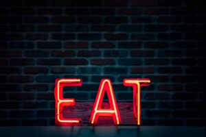 Eating Lunch in Recovery [Image description: Neon Light spelling "EAT"] Depicts the instruction for a person in eating disorder recovery to eat lunch.